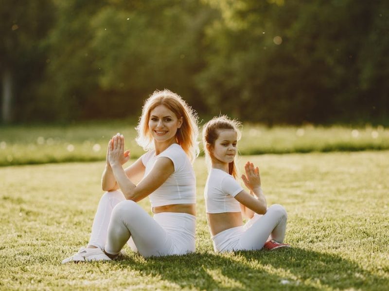 Mother and daughter practicing yoga in matching outfits on grass outdoors, enjoying a sunny day.